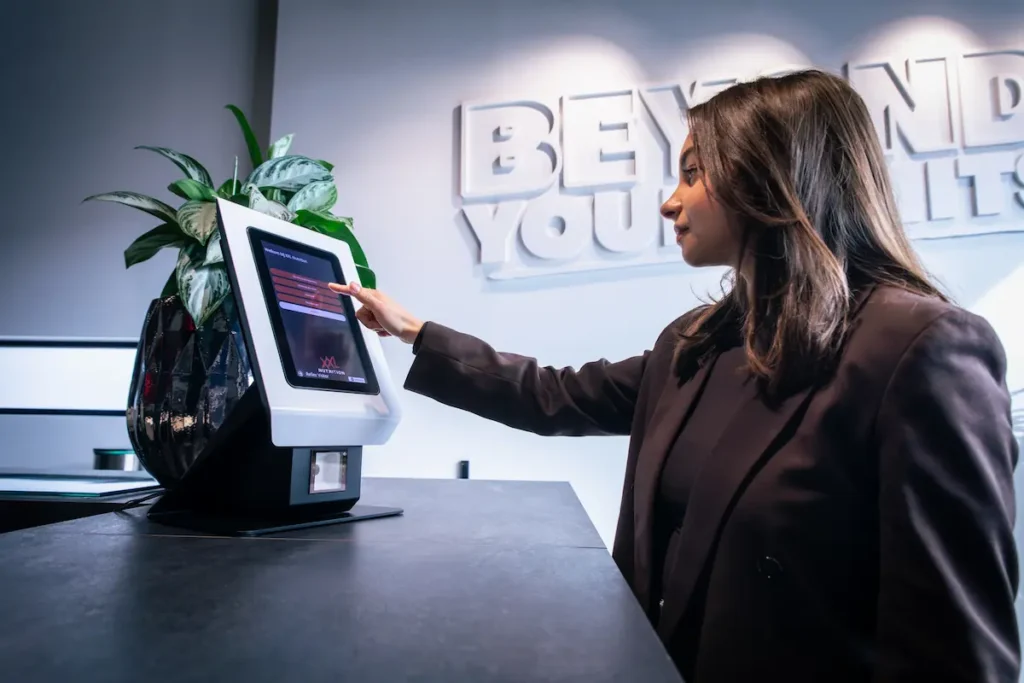 Een vrouw bij een aanmeldzuil voor bezoekersregistratie met digitale receptie