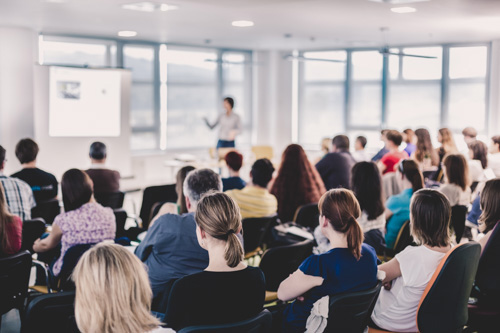 Een groep mensen luistert naar een presentatie in een conferentiezaal.