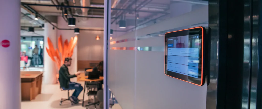 Een moderne kantoorruimte met een zaaldisplay op een glaswand en mensen die in de achtergrond vergaderen.