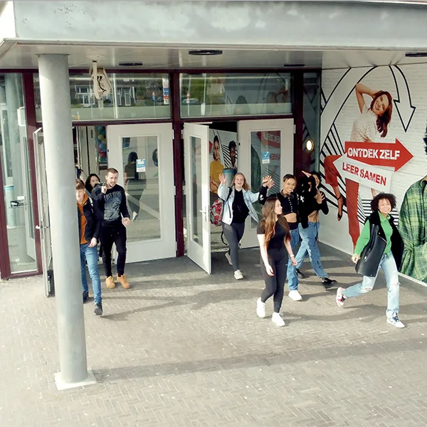 Een groep studenten loopt lachend een schoolgebouw uit met een kleurrijke muurschildering.